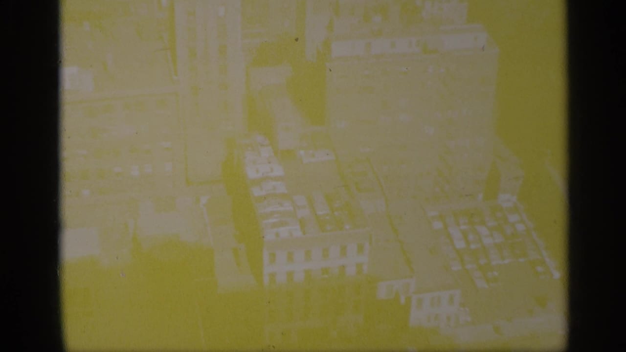 Faint yellow-tinted aerial view of city buildings and rooftops.