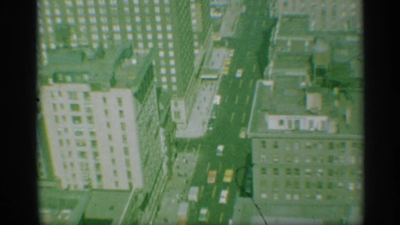 1959 New York aerial view of a long avenue, yellow taxis, cars, rooftops, and a light-colored high-rise facade.