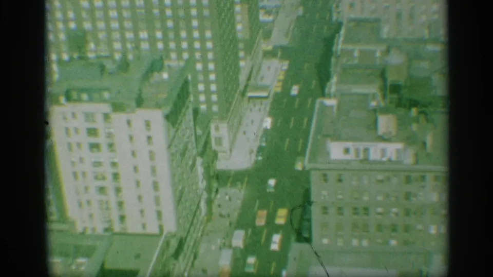 1959 New York aerial view of a long avenue, yellow taxis, cars, rooftops, and a light-colored high-rise facade.