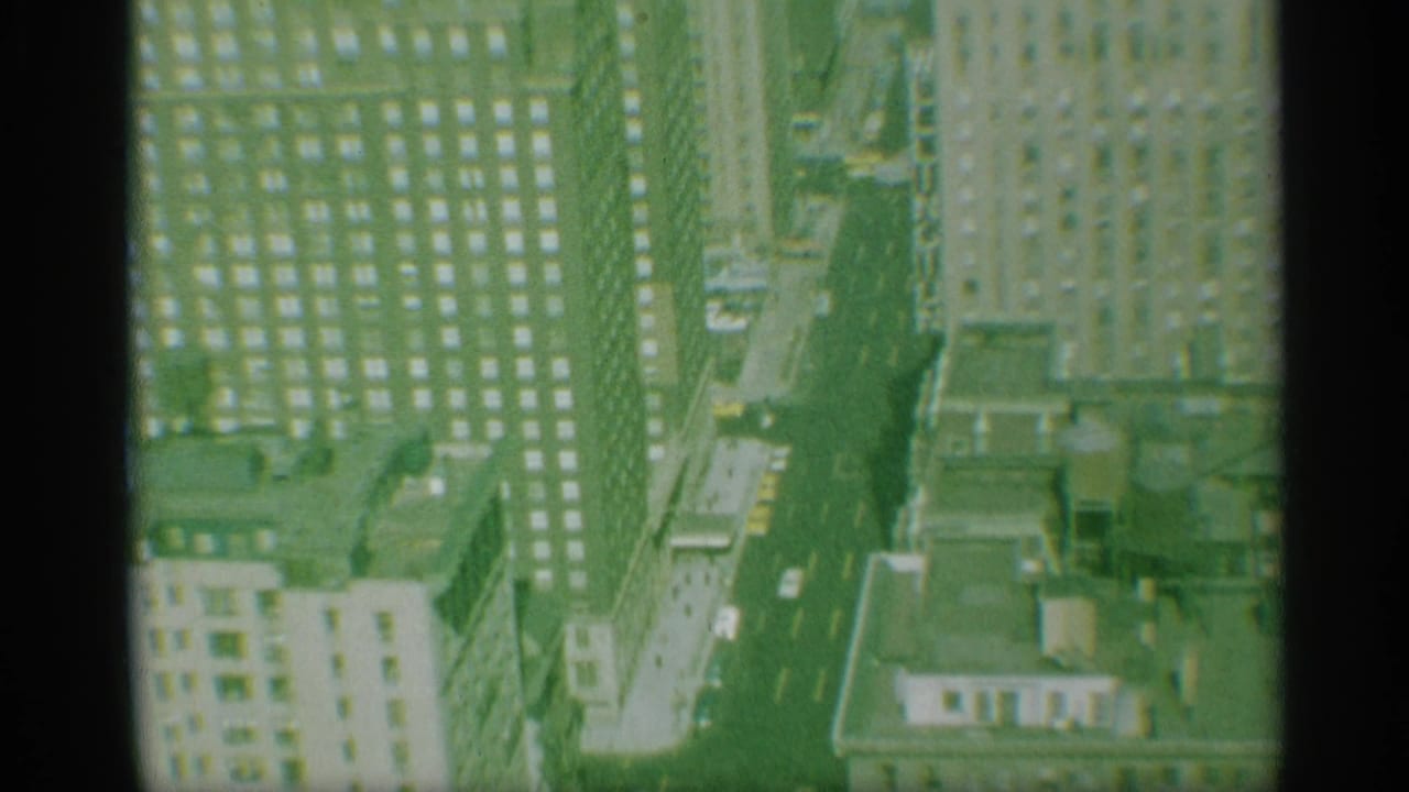 Late-1950s New York overhead view with yellow taxis, cars, tall facades, rooftop details, and green-tinted 8mm texture.