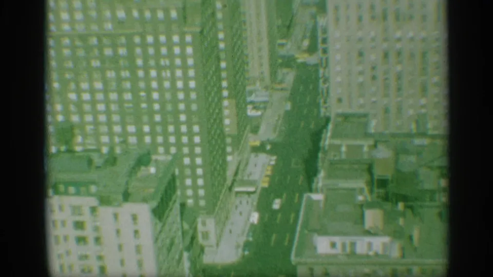 Late-1950s New York overhead view with yellow taxis, cars, tall facades, rooftop details, and green-tinted 8mm texture.