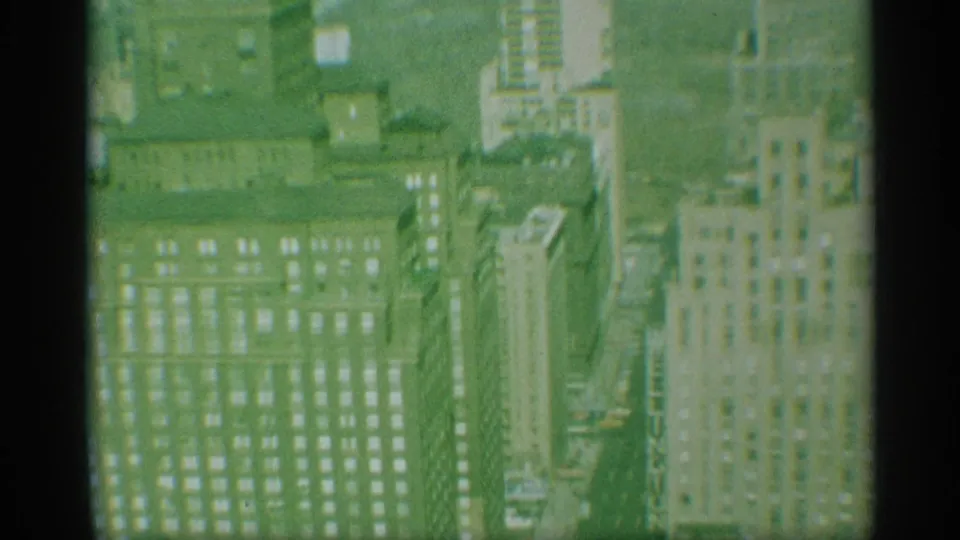 1959 New York frame looking down across Manhattan office buildings, rooftops, and tightly packed city blocks.