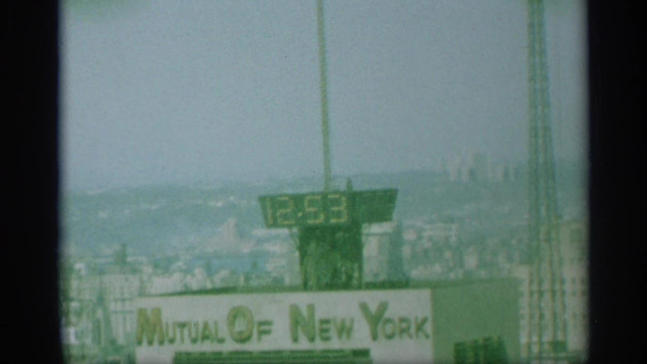1959 New York frame showing a rooftop digital clock reading 12:53 above the Mutual of New York sign and distant skyline.