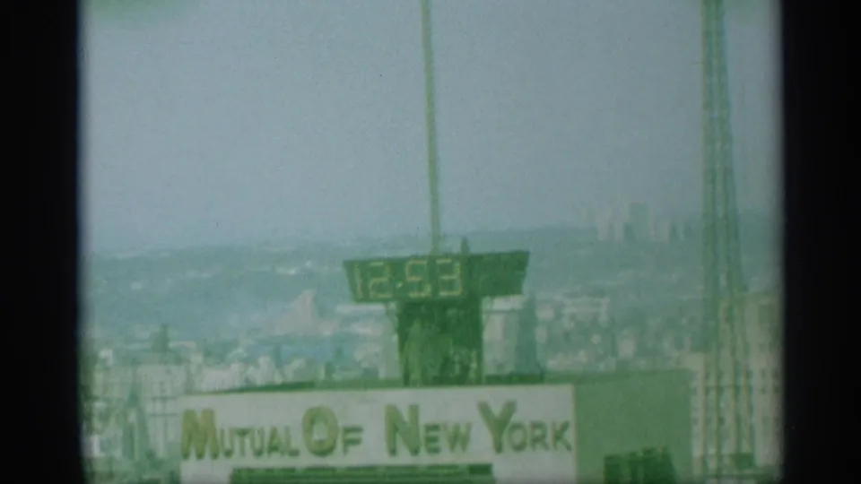 1959 New York frame showing a rooftop digital clock reading 12:53 above the Mutual of New York sign and distant skyline.