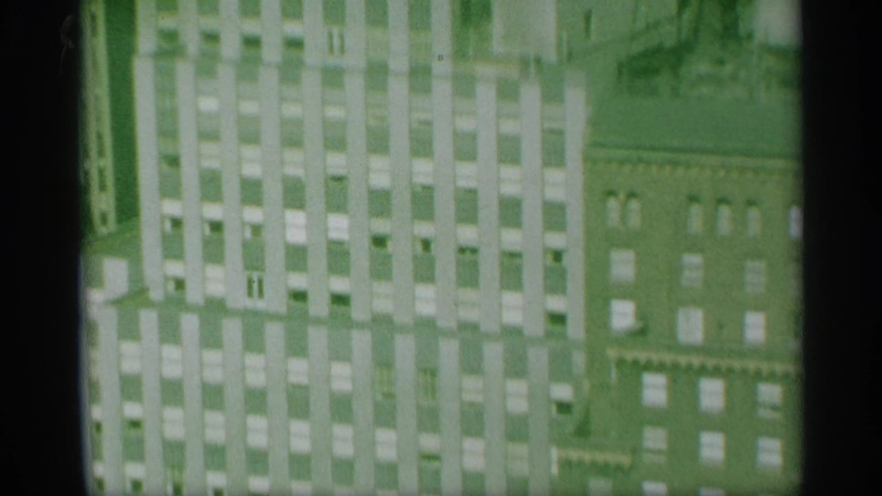 Green-tinted 8mm frame showing the Mutual of New York building facade beside an older brick structure with repeated windows.