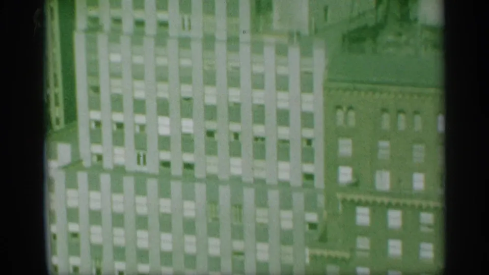 Green-tinted 8mm frame showing the Mutual of New York building facade beside an older brick structure with repeated windows.