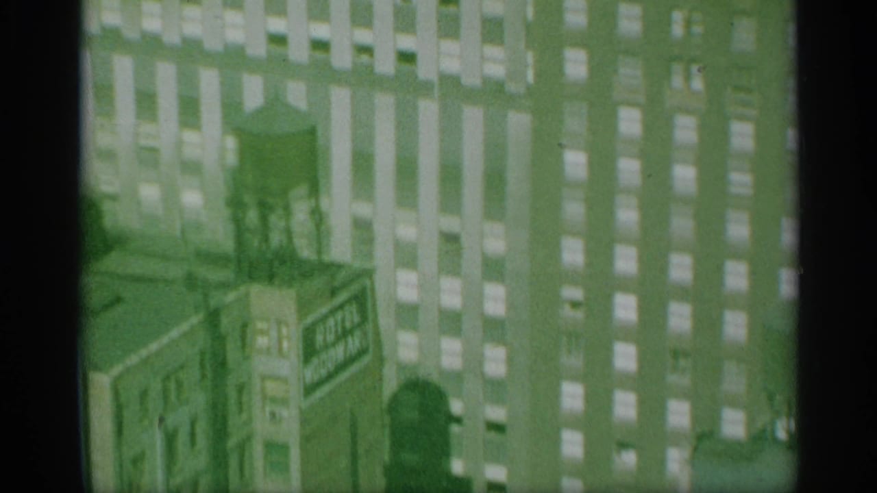 1959 New York home-movie frame showing the tower facade, a rooftop water tank, and adjacent urban buildings under a green film cast.
