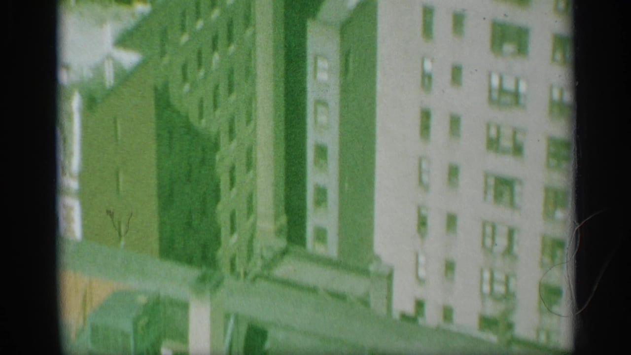 Aerial view between tall buildings with bright facades and shadowed gaps.