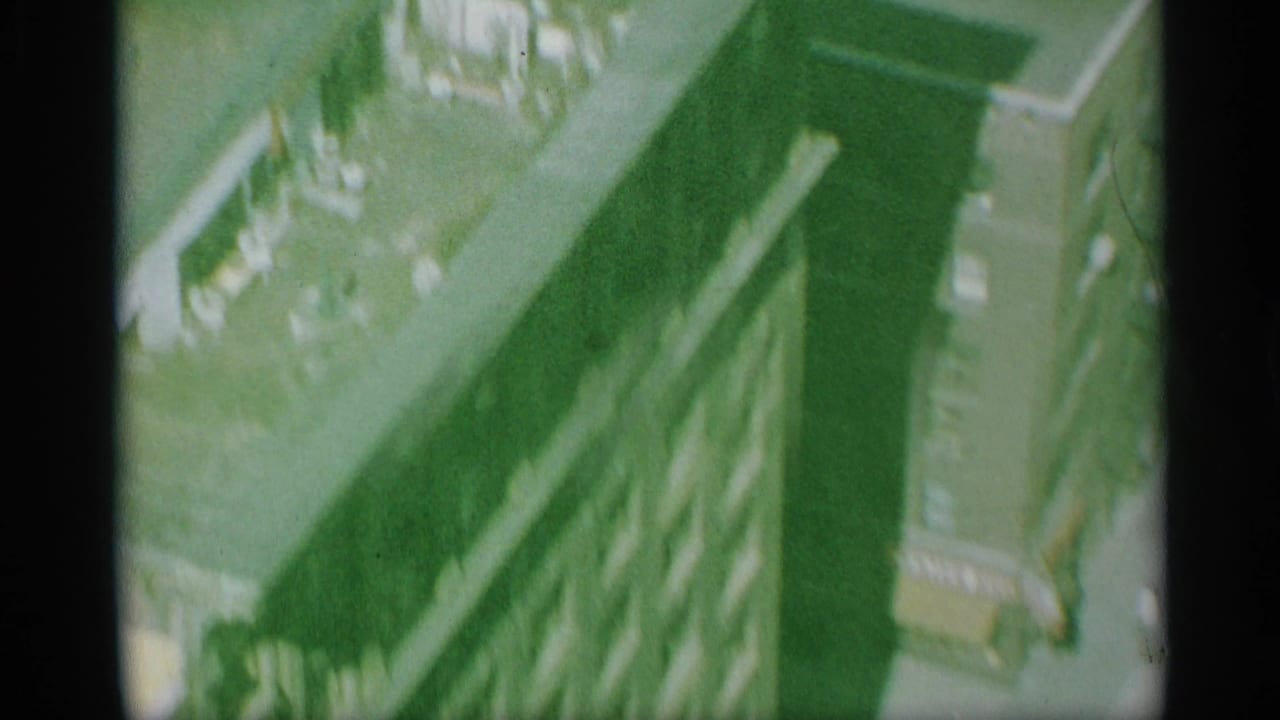 1959 New York 8mm frame with an oblique aerial view over rooftops, building shadows, and a narrow street corridor.