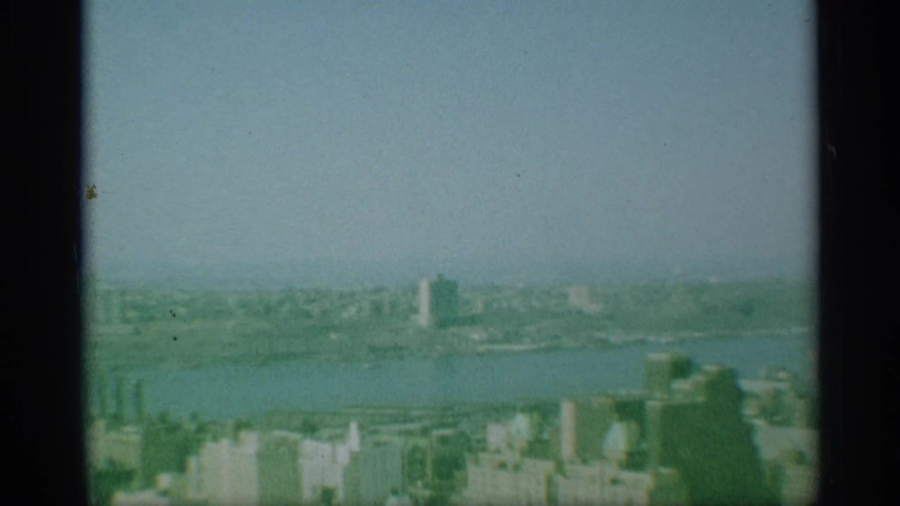 Soft aerial view of a city skyline across a wide river under a hazy sky.