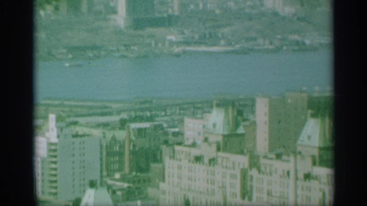 1959 New York aerial view of rooftops, mid-rise buildings, and a riverfront area, seen through grainy 8mm color film.