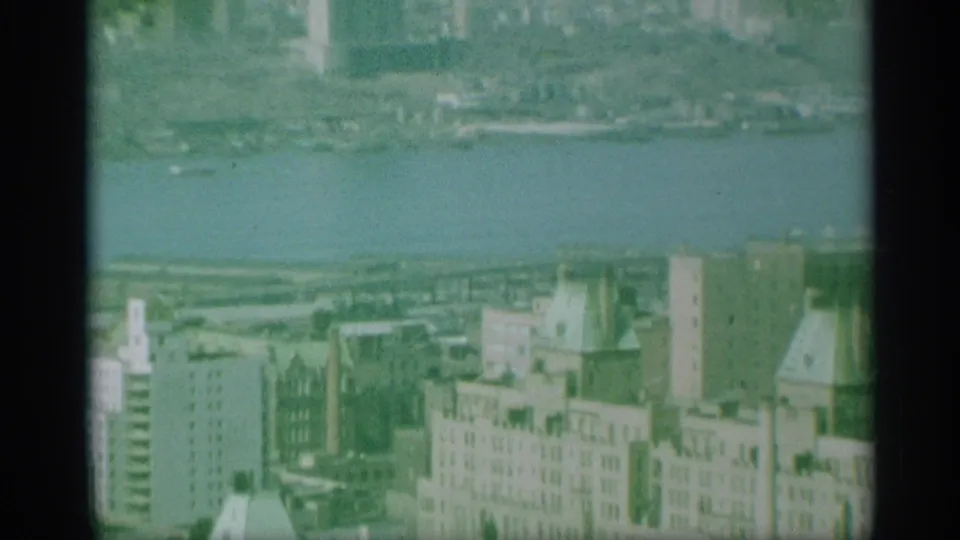 1959 New York aerial view of rooftops, mid-rise buildings, and a riverfront area, seen through grainy 8mm color film.