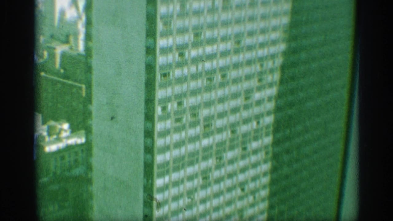 1959 New York 8mm frame with a close, green-tinted view of repeated skyscraper windows and a dark vertical obstruction through the center.