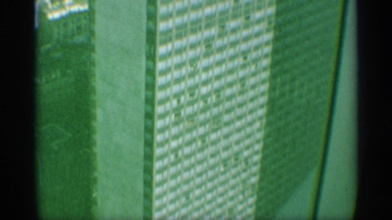 Green-tinted 1959 New York 8mm view of a high-rise facade, showing repeated window rows, a pale structural band, and dark film-edge framing.