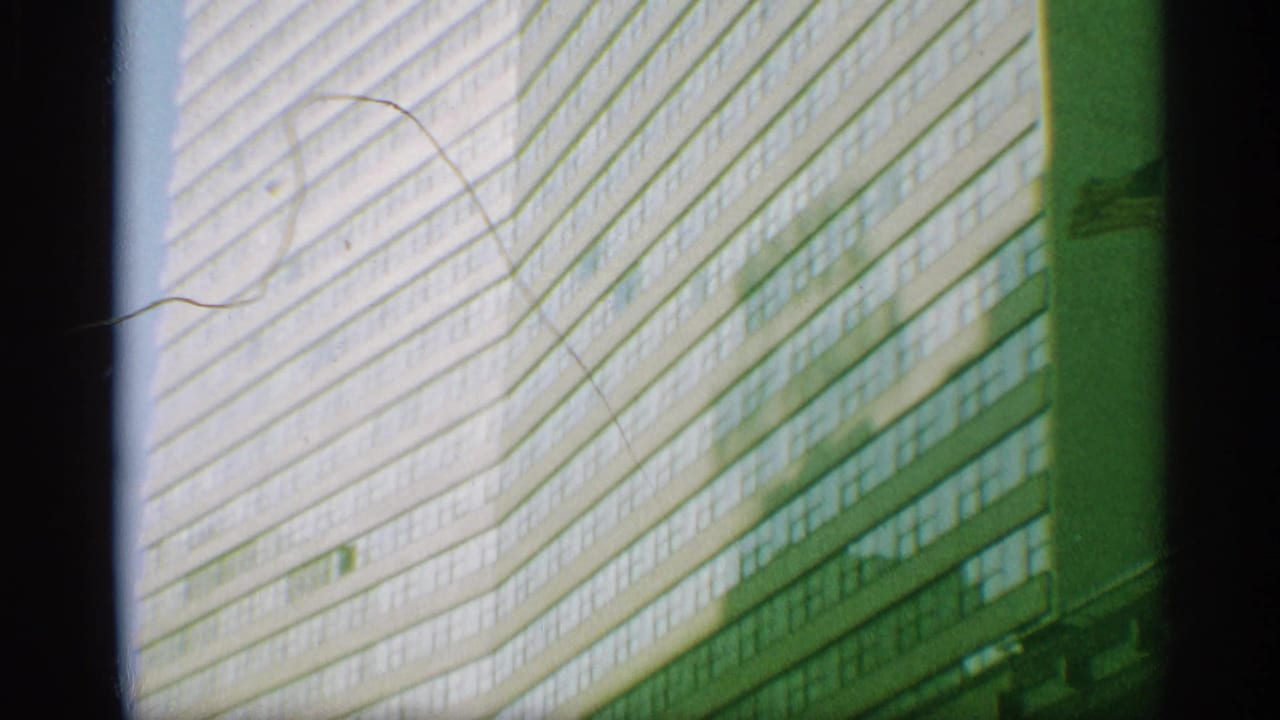 1959 New York 8mm frame showing an angled neighboring high-rise facade with horizontal rows of windows, green tint, and fine film scratches.