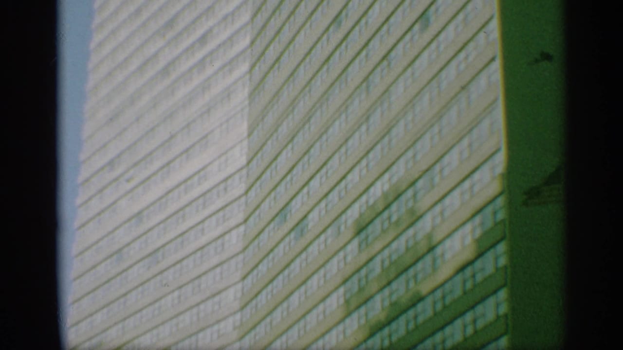 Tall windowed building facade with diagonal patterning and dark film borders.