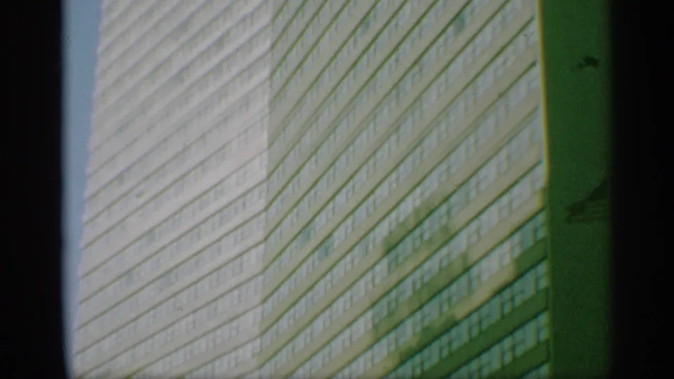 1959 New York 8mm frame looking up at a high-rise office facade with rows of windows and diagonal exterior lines.