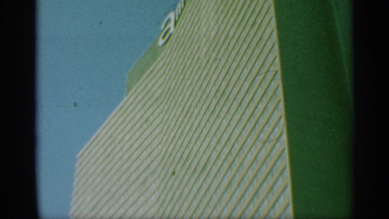 1959 New York frame showing the high-rise corner, gridded windows, blue sky, and partial unidentified lettering near the roofline.