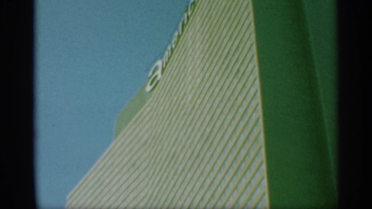 1959 New York 8mm frame showing a low-angle view of a striped skyscraper facade with partial lettering near the top.
