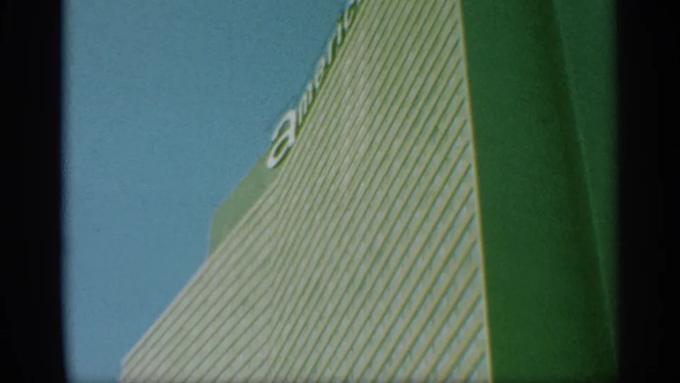 1959 New York 8mm frame showing a low-angle view of a striped skyscraper facade with partial lettering near the top.