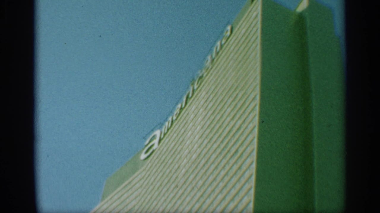 1959 New York home-movie frame of a tall striped building seen from below, with partial American lettering visible near the roofline.