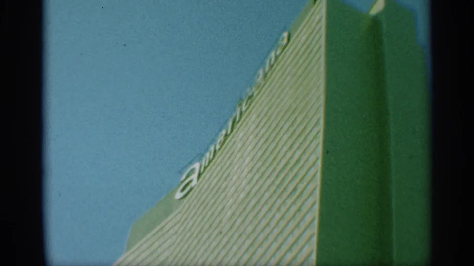 1959 New York home-movie frame of a tall striped building seen from below, with partial American lettering visible near the roofline.