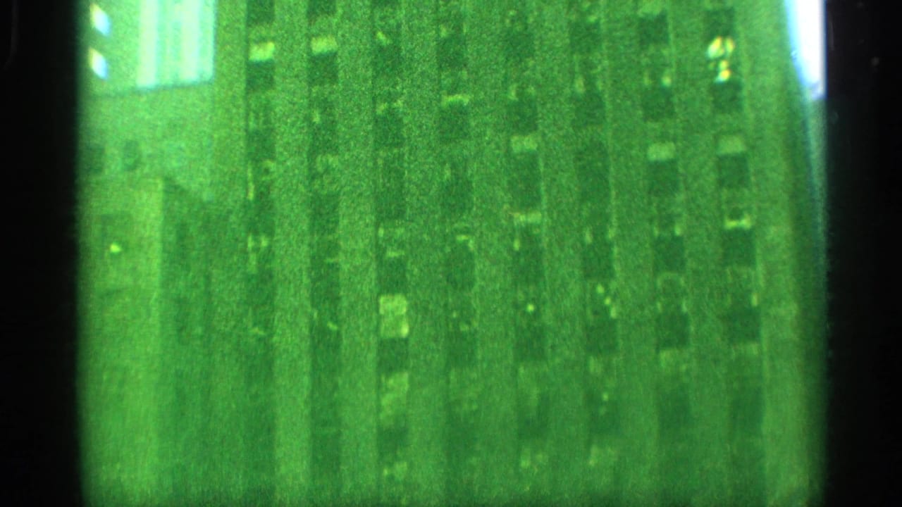 Green-tinted 8mm frame showing reflected or seen-through city building shapes, with a bright rectangular highlight near the top.