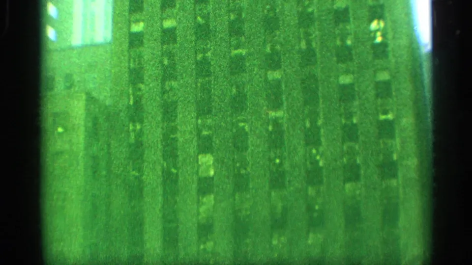 Green-tinted 8mm frame showing reflected or seen-through city building shapes, with a bright rectangular highlight near the top.