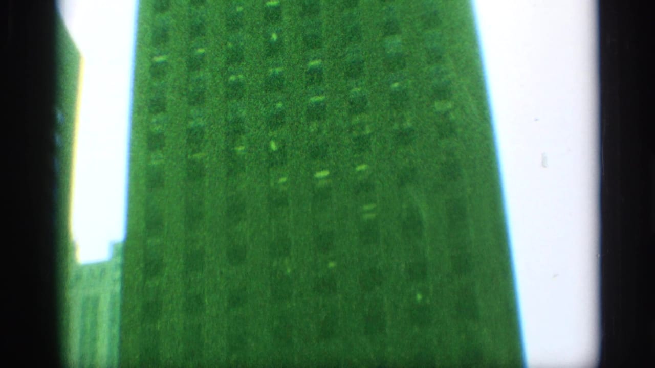 Low-angle 8mm frame with green skyscraper surfaces, a dark central border, and pale sky in the background.