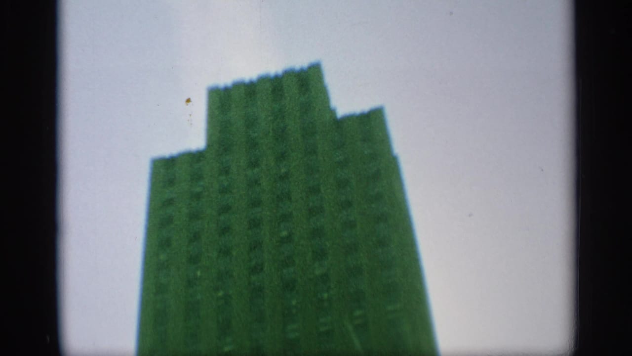 End frame of the upward pan showing the stepped top of a green-tinted Manhattan skyscraper against pale sky.