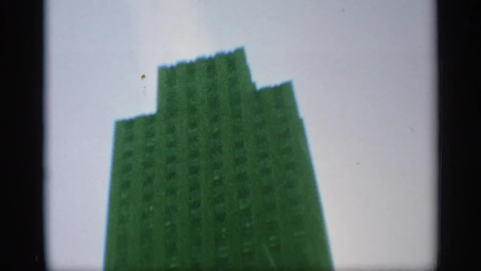 End frame of the upward pan showing the stepped top of a green-tinted Manhattan skyscraper against pale sky.
