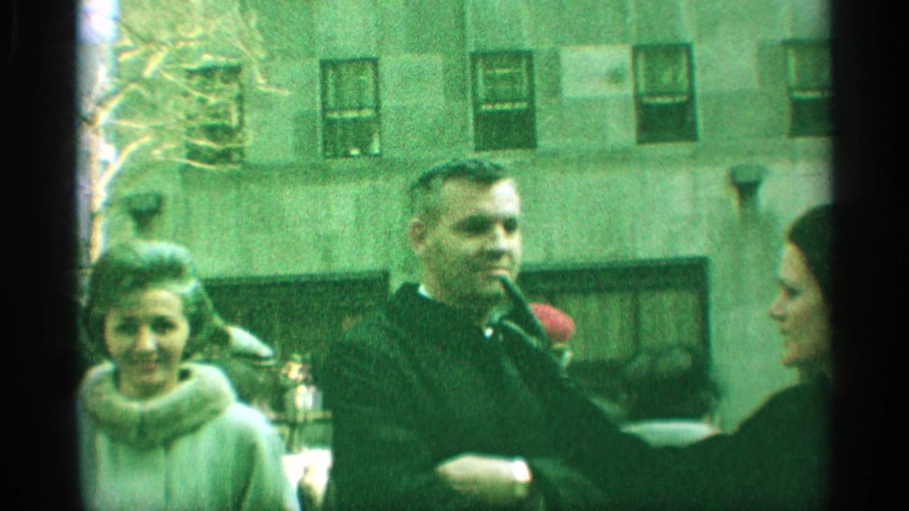 1959 New York street frame with a man in a dark coat, a woman in a light fur-collar coat, and other pedestrians nearby.