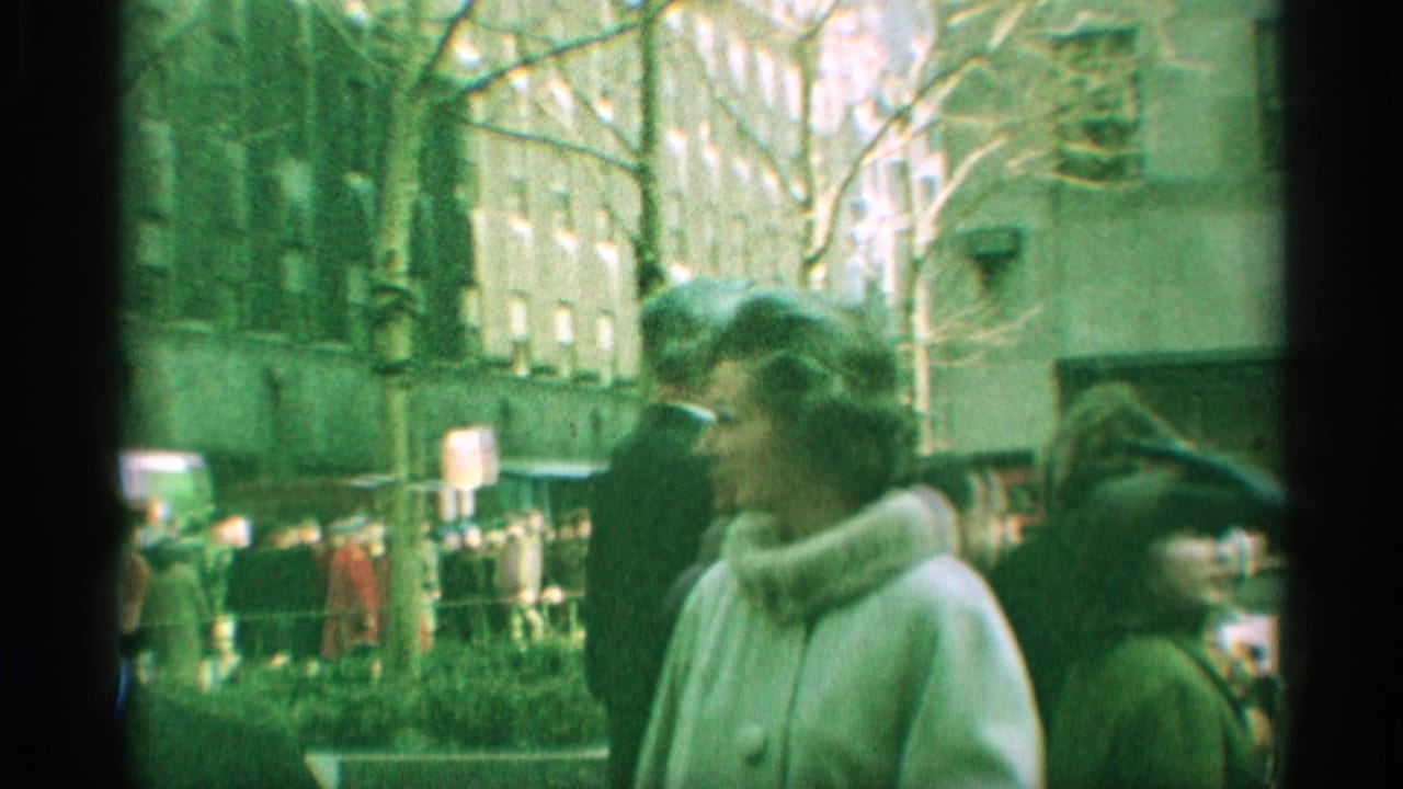 1959 New York home-movie frame showing pedestrians in winter coats walking beside leafless trees and an urban building.