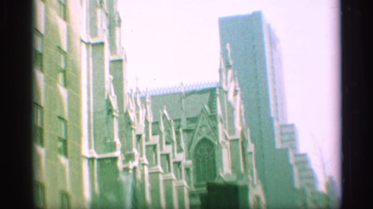 1959 New York home-movie frame showing a Gothic cathedral facade with pointed arches and neighboring urban buildings.