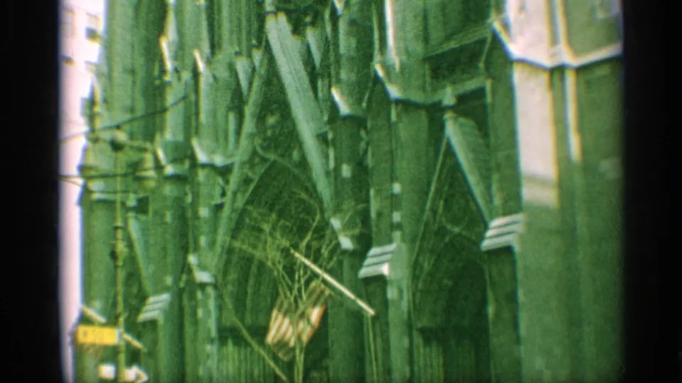 1959 New York 8mm frame showing Gothic entrance details, stone arches, and an American flag near the cathedral facade.