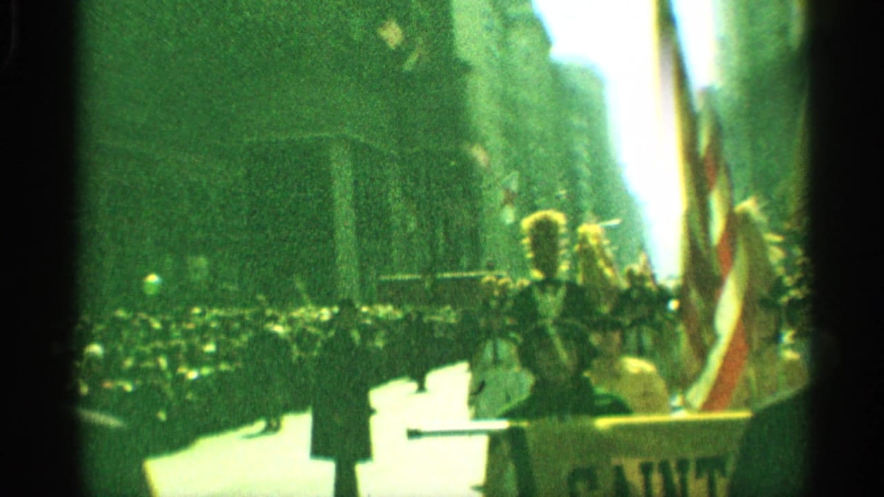 1959 New York 8mm frame of a drum major leading or standing near flags as spectators watch from the sidewalk during a bright street parade.