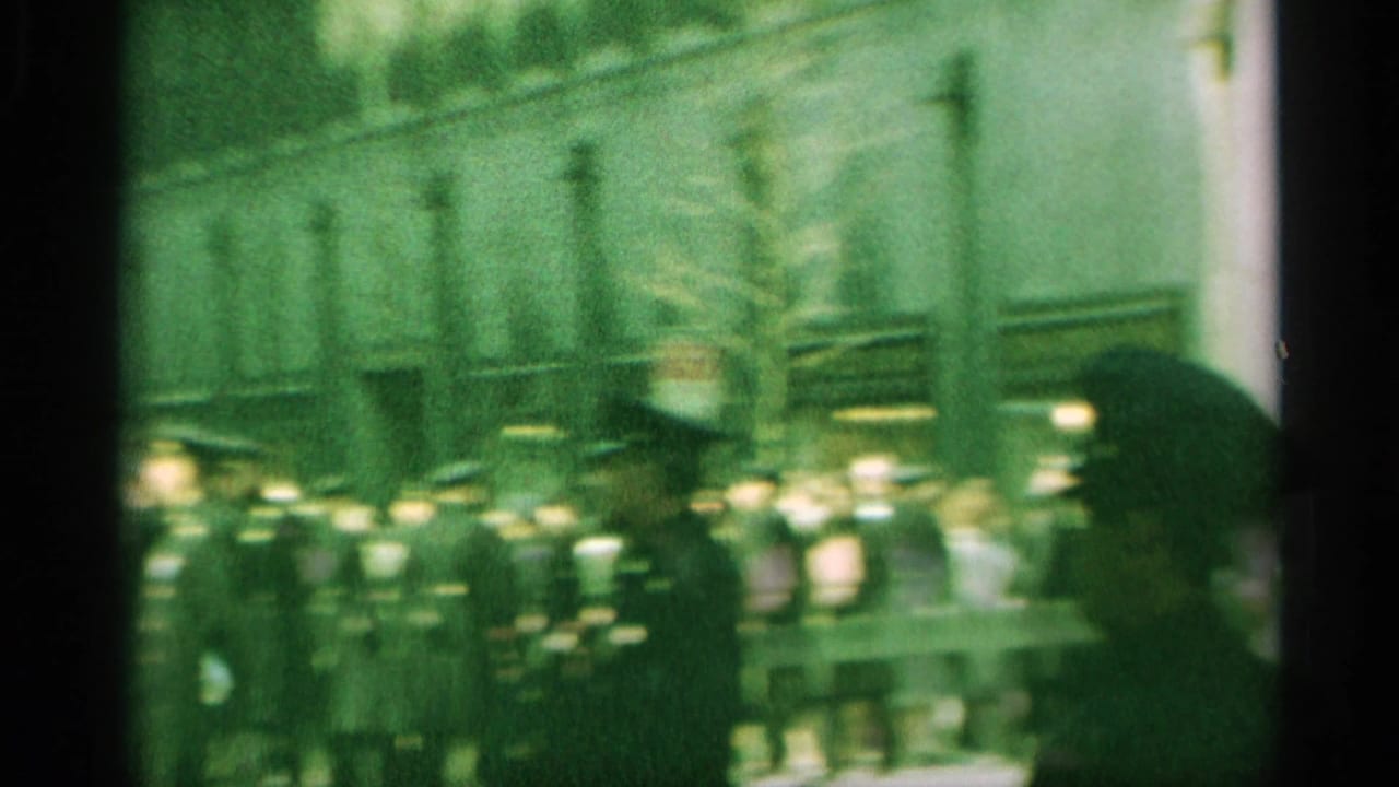 1959 New York home-movie frame showing spectators and uniformed officers gathered along a city street.