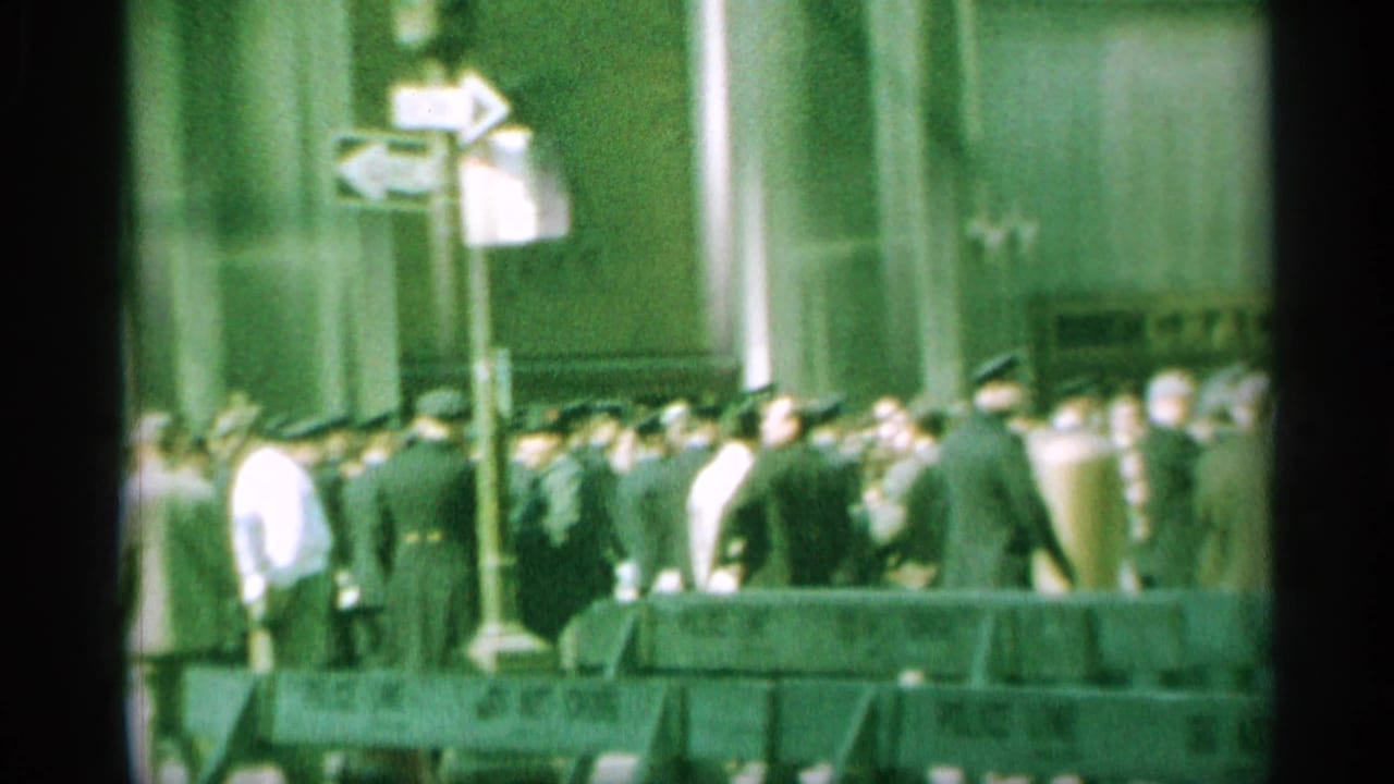 1959 New York home-movie frame showing officers, spectators, street-direction signs, and a vintage car.