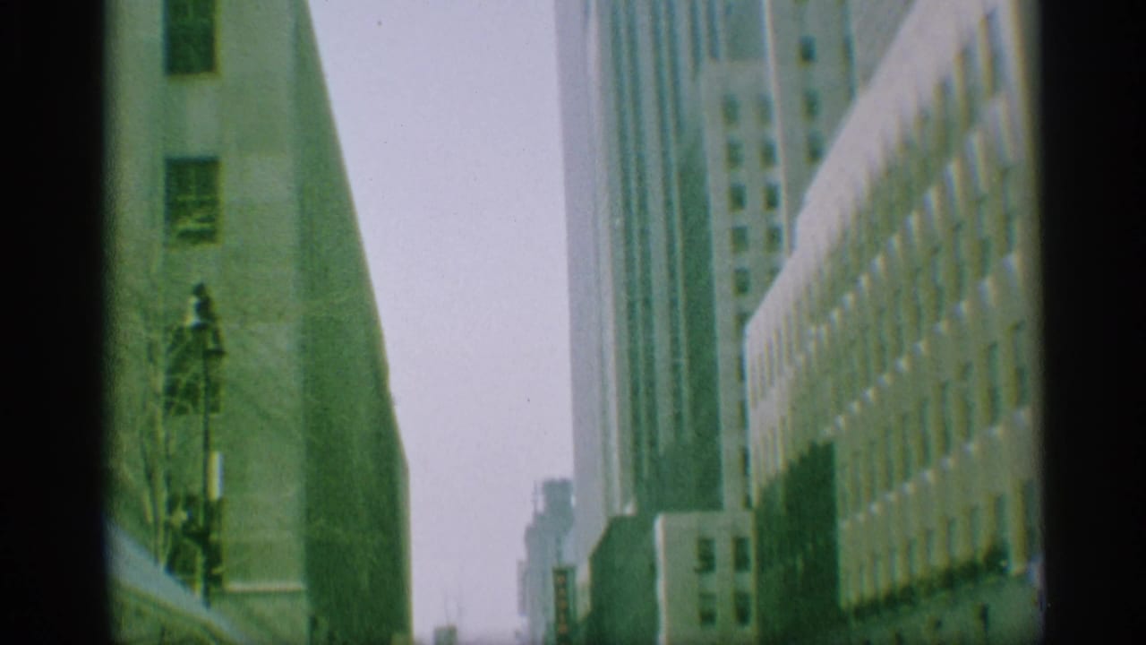 1959 New York home-movie view of tall downtown buildings, a streetlamp, and distant traffic after the procession leaves frame.