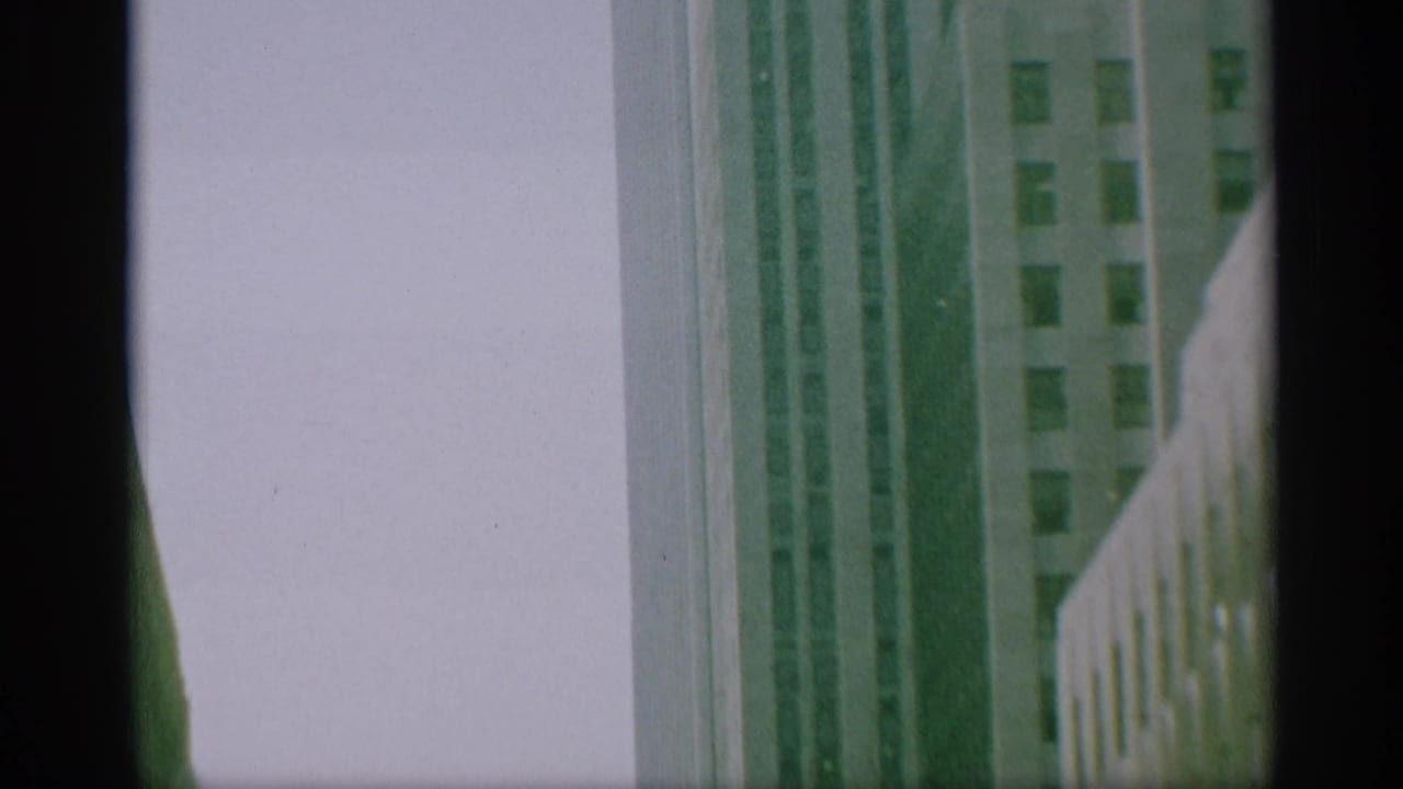 Final 1959 New York frame with high-rise building facades, pale sky, and a dark edge from the 8mm home-movie frame.