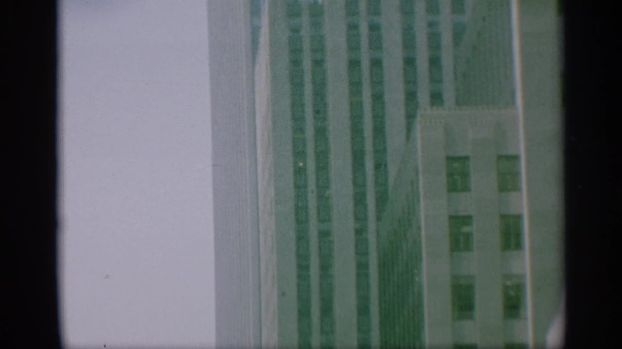 1959 New York 8mm frame showing a tall skyscraper facade rising against pale sky, with soft focus and dark film border.
