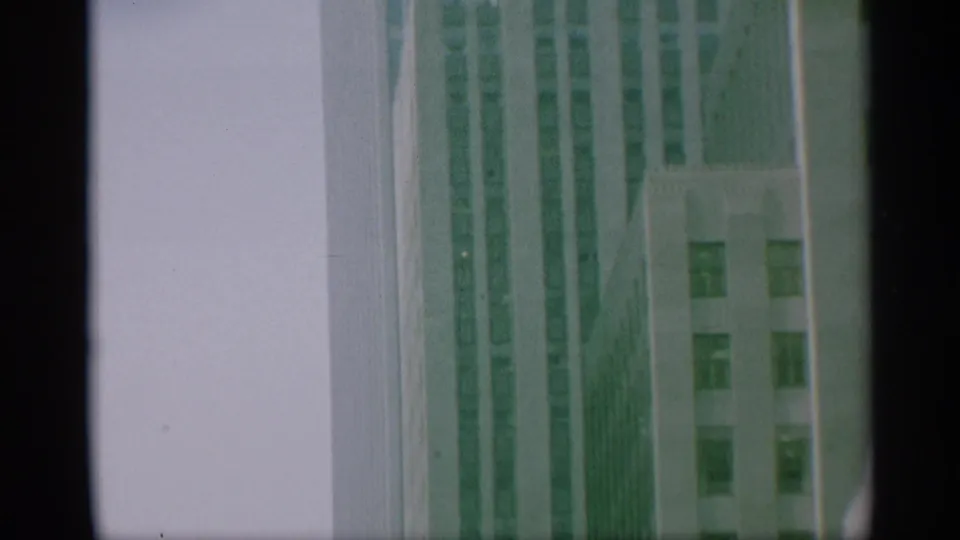 1959 New York 8mm frame showing a tall skyscraper facade rising against pale sky, with soft focus and dark film border.