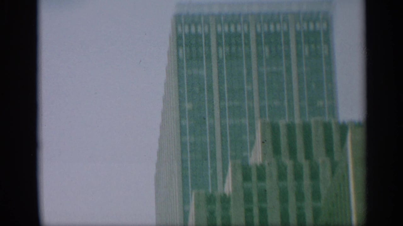 1959 New York 8mm frame showing the upper portion of a skyscraper and neighboring building surfaces under a pale sky.