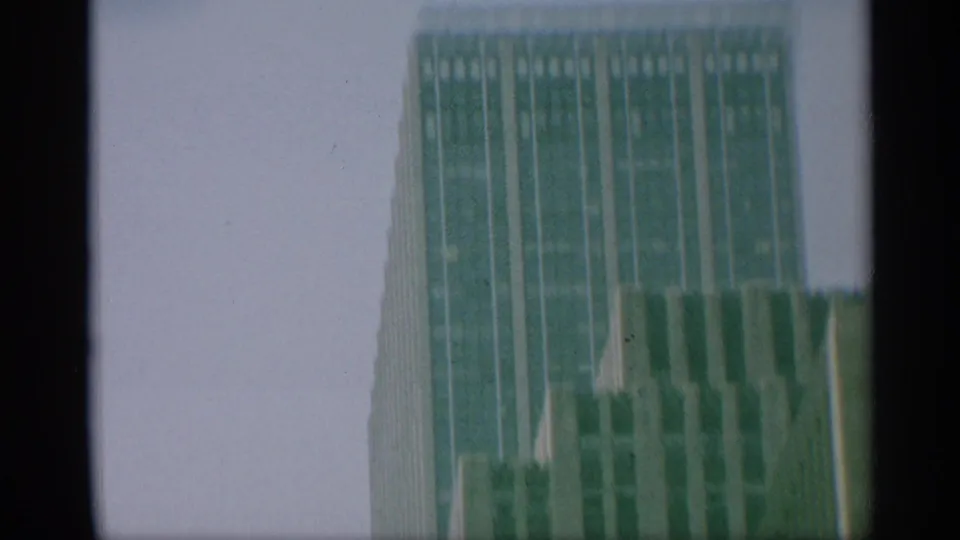 1959 New York 8mm frame showing the upper portion of a skyscraper and neighboring building surfaces under a pale sky.