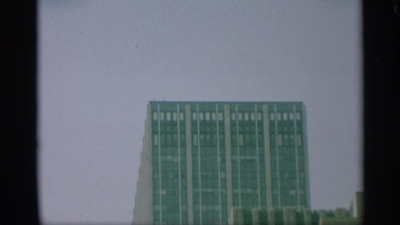 1959 New York 8mm frame with the top of a rectangular high-rise set low in the frame beneath a large pale sky.