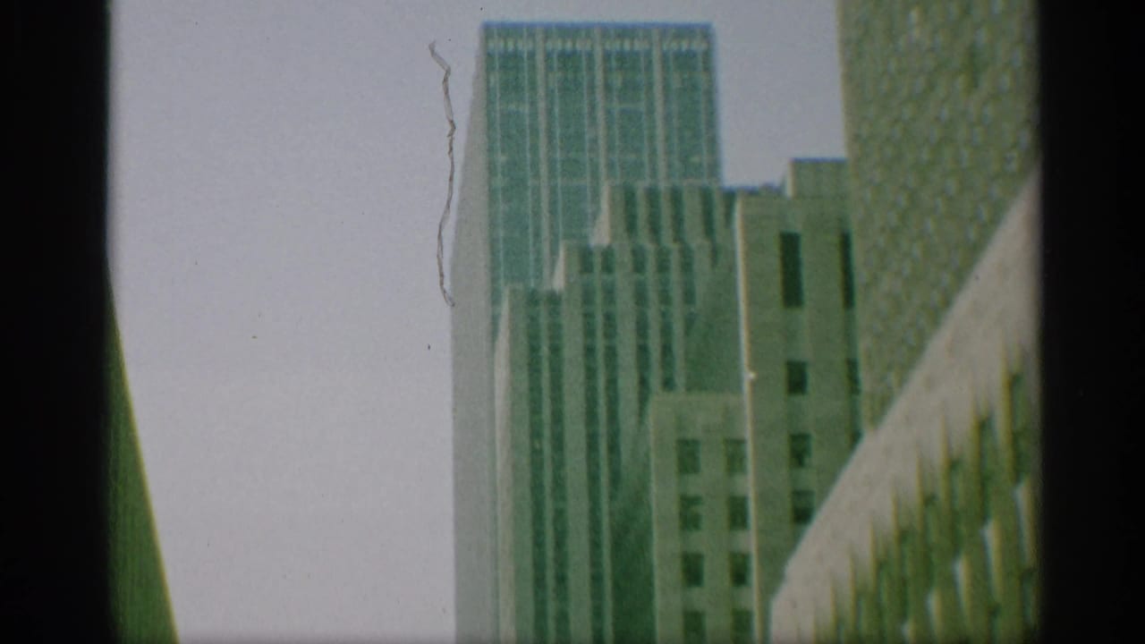 1959 New York 8mm frame looking up at tall office buildings with gridded windows and dark frame borders.