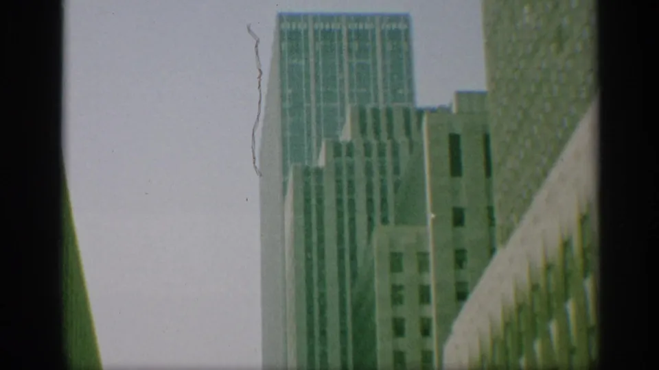 1959 New York 8mm frame looking up at tall office buildings with gridded windows and dark frame borders.