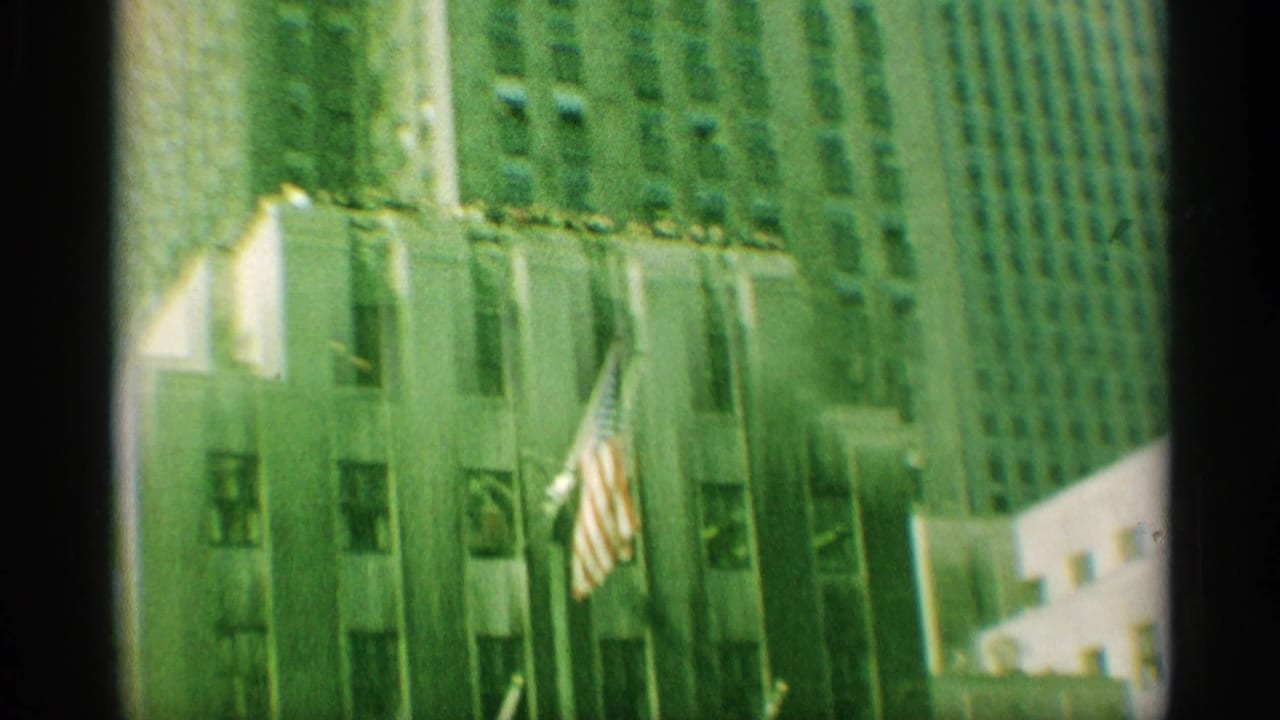 1959 New York frame showing an American flag on a building facade amid neighboring high-rises.