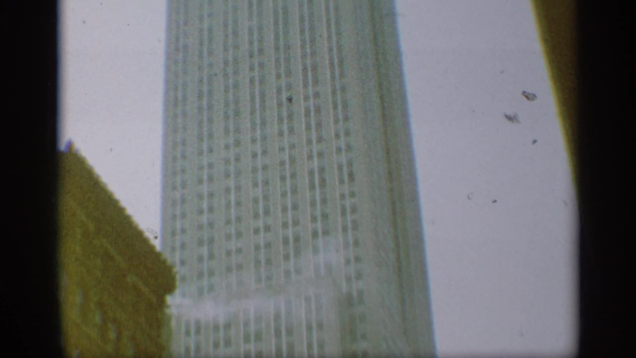 1959 New York home-movie view looking up at a tall skyscraper, with pale sky, edge shadows, and visible film wear.