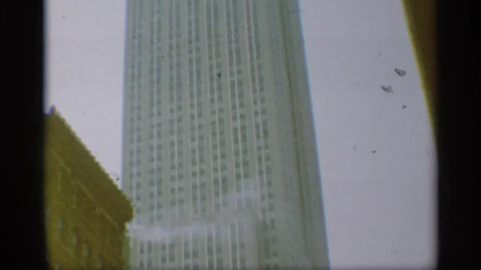 1959 New York home-movie view looking up at a tall skyscraper, with pale sky, edge shadows, and visible film wear.